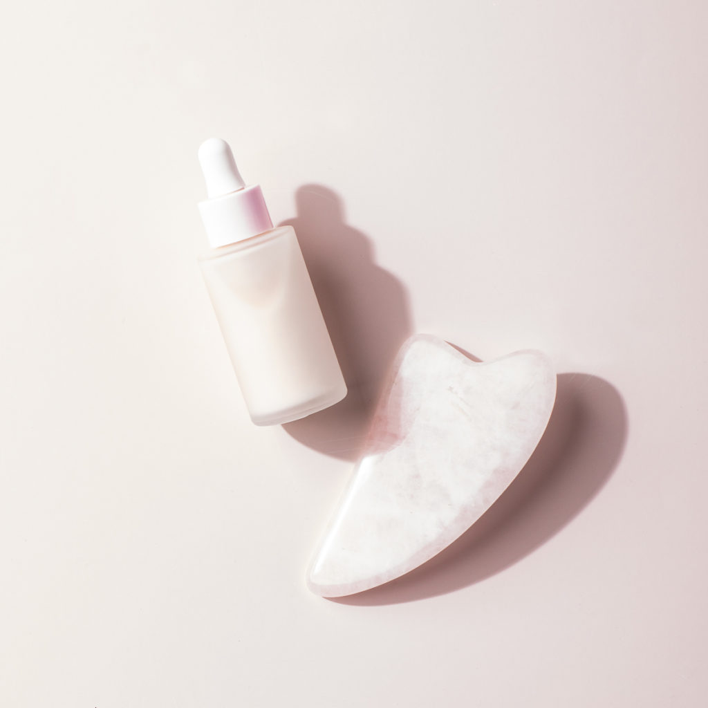 A bottle of serum and a gua sha stone used for health and wellness